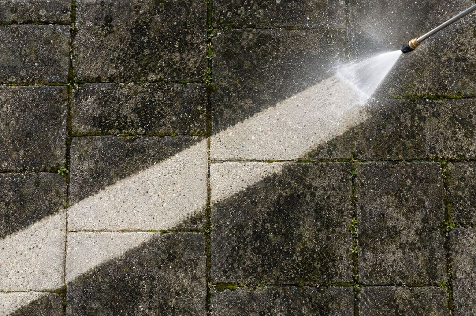 A clean stripe pressure washed across grimy concrete pavers
